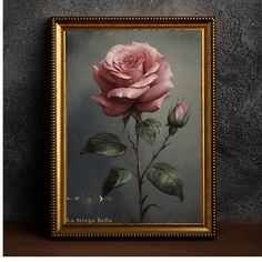 a painting of a pink rose in a gold frame on a table next to a gray wall