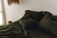 an unmade bed with dark green sheets and pillows