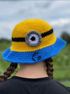 a woman wearing a yellow and blue crocheted hat with an eyeball on it