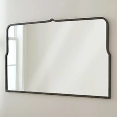 a mirror hanging on the wall in front of a window with white walls and windowsill