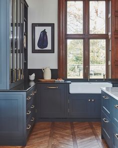 a kitchen with wooden floors and blue cabinets in front of a window that has large windows