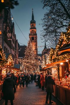 people are walking through an outdoor market with christmas lights on the trees and buildings in the background