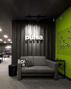 an office lobby with green walls and black curtains, grey couches, and tables