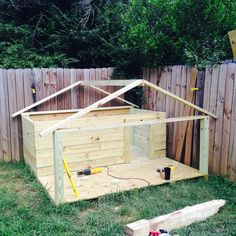 a wooden shed with the roof up and tools on the ground in front of it