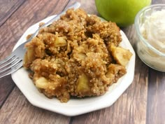 a white plate topped with apple crisp next to a bowl of whipped cream and an apple