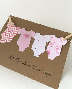 a brown card with pink and white onesuits hanging from clothes pins