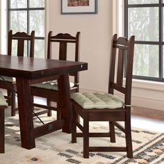 a dining room table with four chairs and a rug in front of the window,