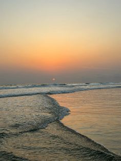 the sun is setting over the ocean with waves coming in to shore and people walking on the beach