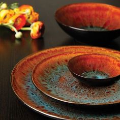 two brown and orange plates sitting on top of a wooden table next to a flower