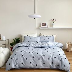 a bed with blue and black polka dot comforter in a white room next to a plant