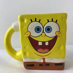 a yellow spongebob coffee mug with blue eyes and mouth wide open, sitting on a white surface