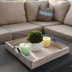 a tray with two candles and a potted plant on it sitting on a couch