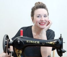 a woman sitting at a sewing machine with her hand on her chin and looking into the camera