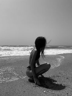 a woman kneeling down on top of a sandy beach