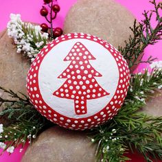 a red and white painted rock with a christmas tree on it next to some rocks