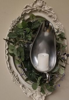 a candle and some plants in a white bowl with a spoon hanging on the wall