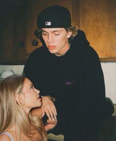 a young man and woman sitting next to each other in a kitchen with wooden cabinets