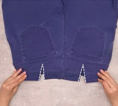 two hands are holding the back of a pair of blue jeans with white zippers