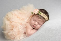 a newborn baby girl wearing a flower headband and sleeping on her tutue