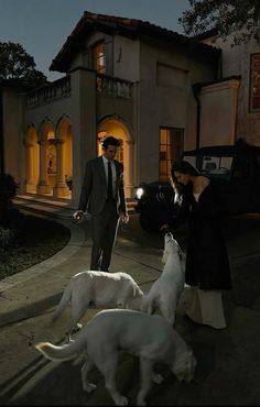 a man and woman are walking their dogs in front of a house at night with the lights on