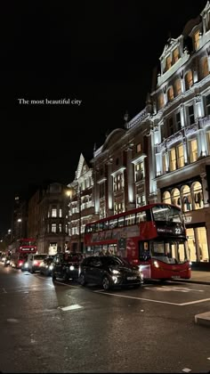 a red double decker bus driving down a street next to tall buildings in the night