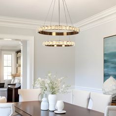 a modern chandelier hangs above a dining room table with white chairs and vases