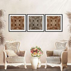 three framed art prints on the wall above two chairs and a vase with flowers in it