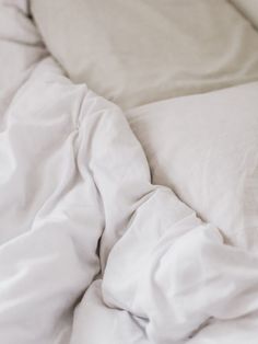 an unmade bed with white sheets and pillows