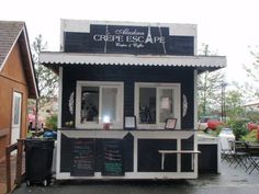 a black and white building with chalkboard writing on the front, along with tables and chairs