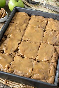 a pan filled with brownies covered in caramel icing next to two bowls of apples