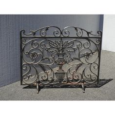 an ornate iron fireplace screen on wheels with flowers and vases in the center, against a gray wall