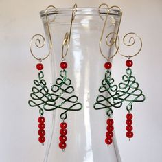 a pair of earrings with red beads and green wire work on the ends, hanging from a glass vase