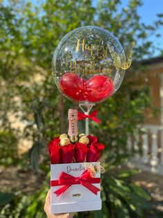 a person holding up a clear balloon with red roses in it and a card that says happy birthday