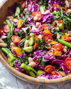 a colorful salad in a wooden bowl on top of a white table cloth next to a fork