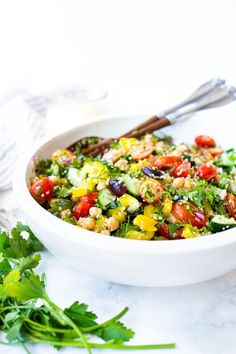 a white bowl filled with salad on top of a table next to cilantro