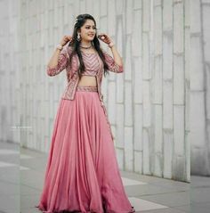 a woman in a long pink skirt and crop top standing next to a white wall