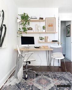 a desk with a computer on top of it next to a chair and potted plant