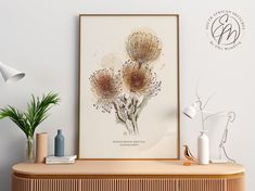 an art print on the wall above a wooden cabinet with vases and plants next to it