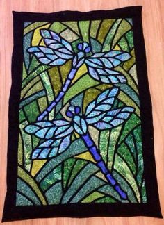 a stained glass window with blue dragonflies on it's back and green leaves in the background