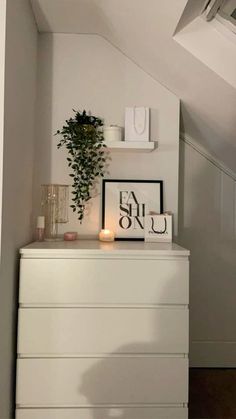 a white dresser sitting under a window next to a plant on top of a wooden floor