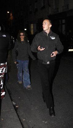 two people walking down the street at night, one is holding his hand out to someone else