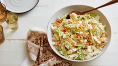 a white bowl filled with coleslaw next to two glasses and napkins on a table