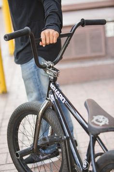 a close up of a person standing next to a bike on the sidewalk with his hand on the handlebars