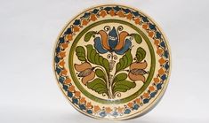 a decorative ceramic plate with flowers and leaves on the rim, painted in blue, green, orange and yellow colors