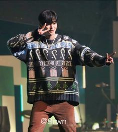 a man standing on top of a stage with his hands up in the air while wearing a sweater