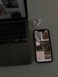 an open laptop computer sitting next to a cell phone and earphones on a table