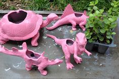 pink dinosaur planters sitting on top of a metal tray next to plants and potted plants