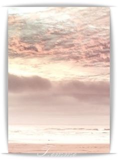 a person walking on the beach in front of an ocean and sky with pink clouds