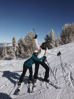 two people on skis in the snow with their arms around each other and trees behind them