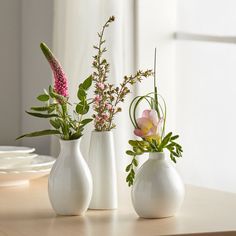 three white vases with flowers in them on a table